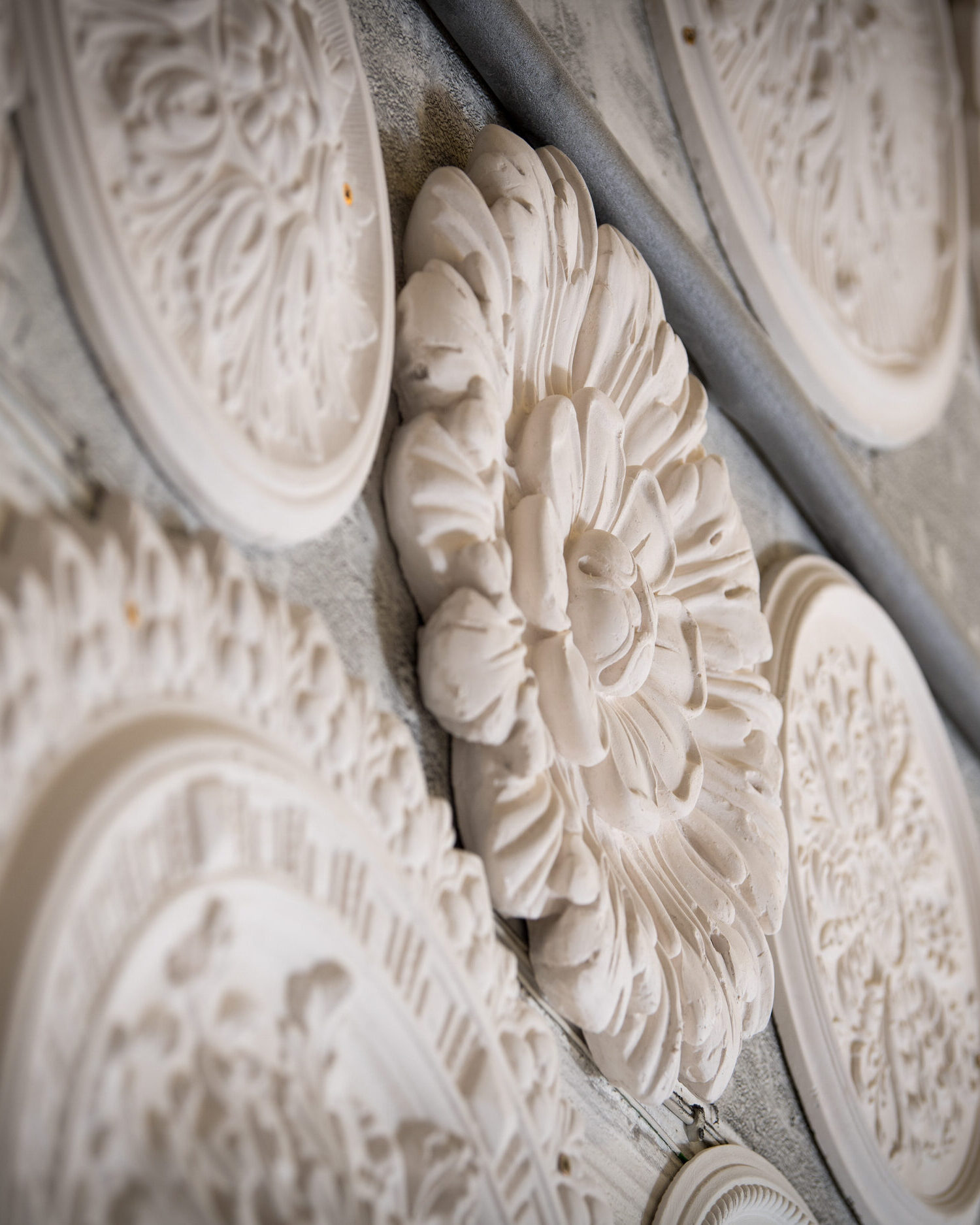 Collection of ornate plaster ceiling roses from historic designs displayed on workshop wall